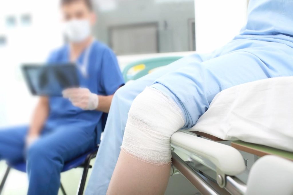 Patient with bandaged knee at urgent care that accepts Ambetter Gulfton, with doctor reviewing X-ray in background