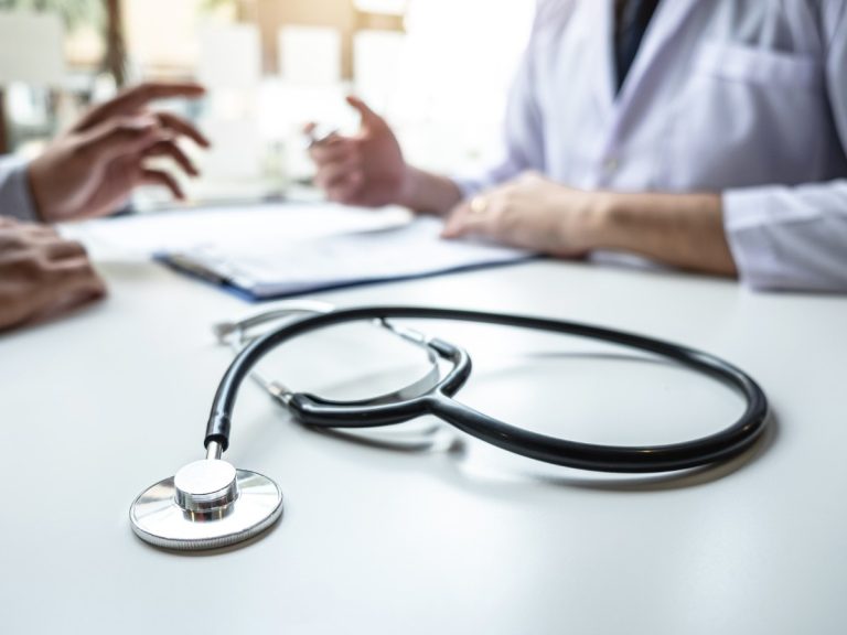 Doctor and patient in consultation with a stethoscope on table at urgent care open now clinic.