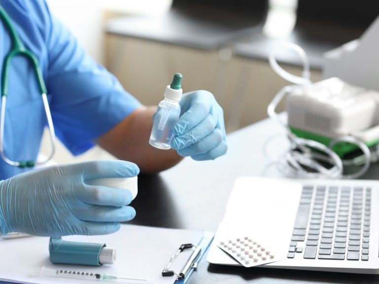 Medical professional preparing medication with a dropper at an Urgent Care Open Now Houston clinic, with a laptop and blister pack of pills on the table.