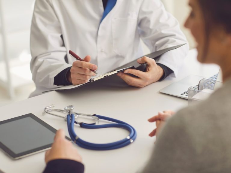 Doctor writing notes at a Walk-In Clinic Ambetter Insurance consultation with a stethoscope and tablet on the table.