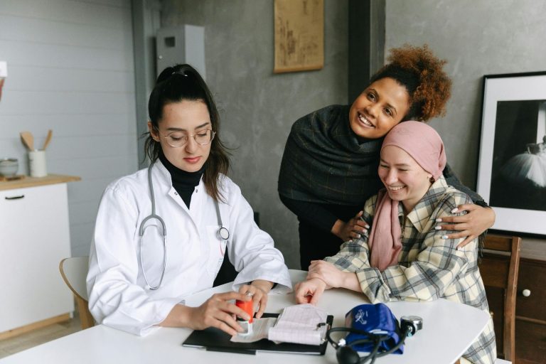 A nurse consults with two smiling female patients, one with a headscarf, suggesting compassionate care.