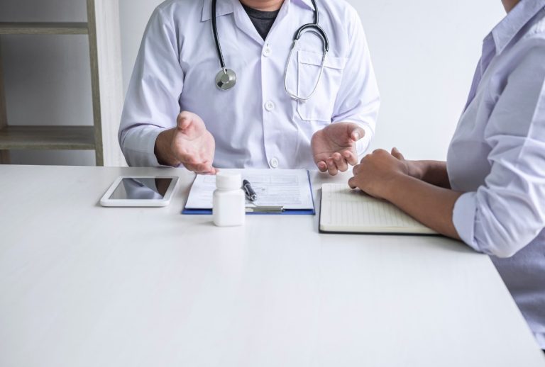 Primary care doctor that takes Ambetter discusses treatment plan with patient using tablet and notes in modern clinic.