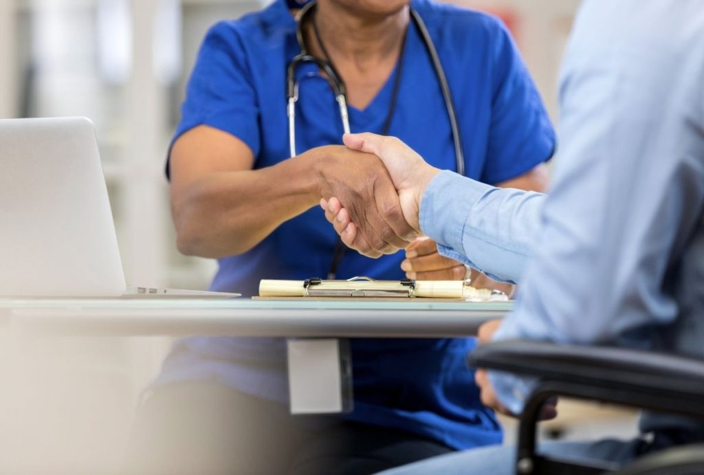 Doctor in blue scrubs shakes hands with patient during clinic consult — Ambetter Accepted Doctors Houston trusted care