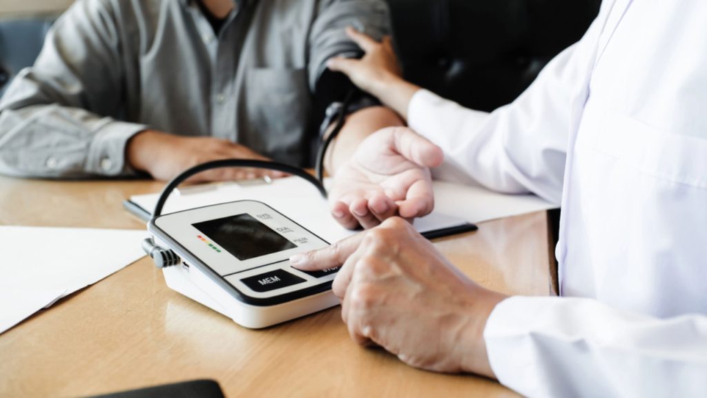 Urgent care services Houston nurse checking patient blood pressure with digital monitor during fast cardiovascular screening and hypertension assessment