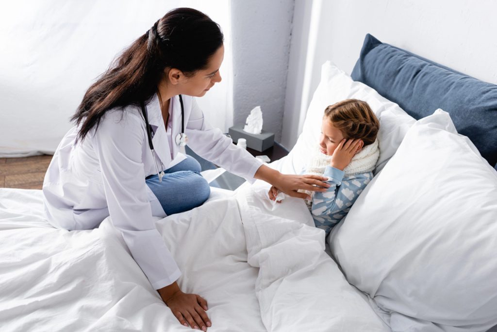 Pediatrician comforting a young girl with an ear infection during a medical visit at an urgent care clinic facility