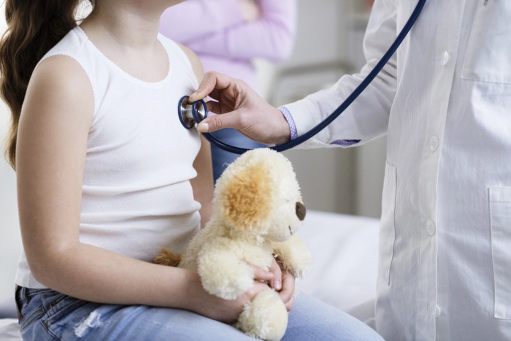 Urgent care services Houston pediatrician listening to child’s chest with stethoscope, comforting teddy bear during gentle health check