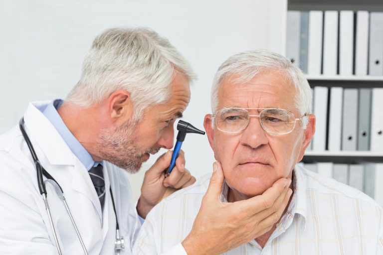 Professional doctor uses an otoscope to examine a senior patient's earache at a local urgent care clinic today