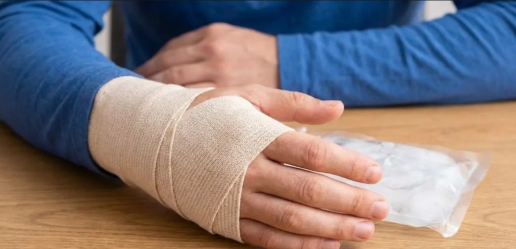 A hand with a wrapped wrist injury rests on a table with an ice pack, a condition treated by a no appointment doctor Houston.