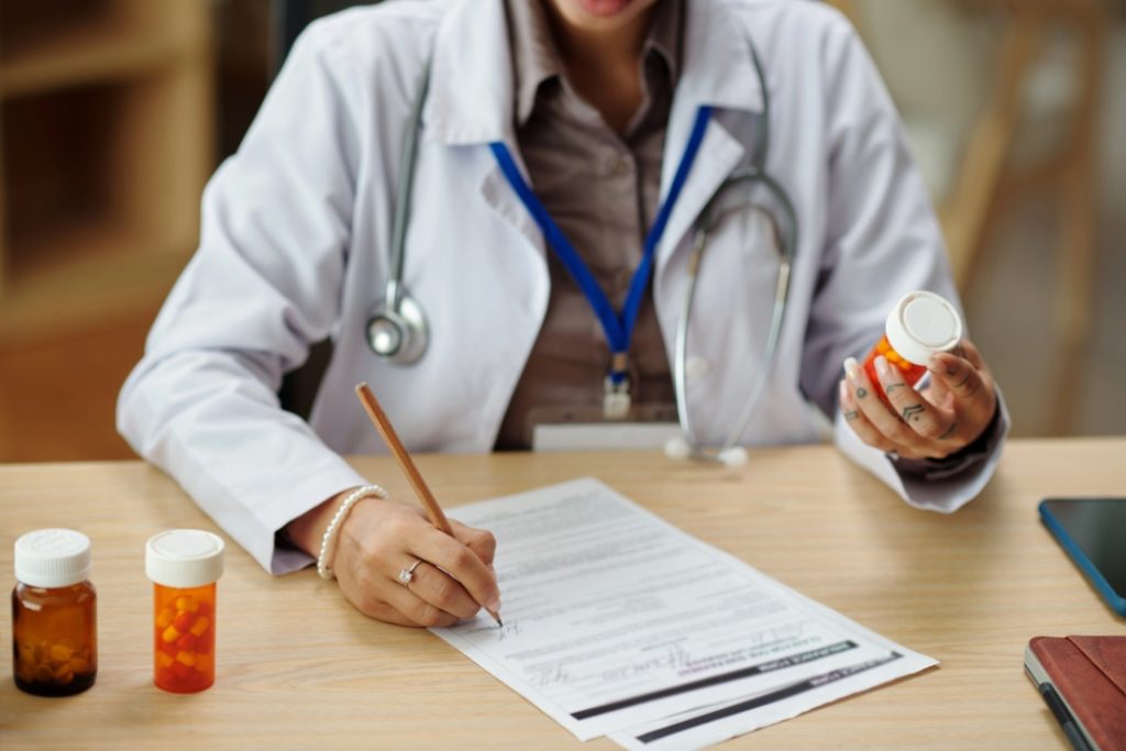 Doctor writing prescription with medication bottles, representing diagnosis and uti treatment houston healthcare solutions