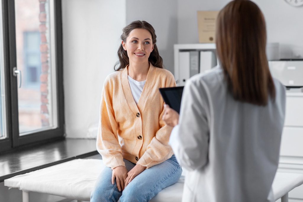 A smiling patient sits on an exam table, consulting with a doctor at an Ambetter approved urgent care houston location.