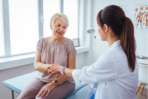 Elderly woman and a compassionate doctor hold hands and talk about health at a top-rated facility for an annual physical exam Houston.