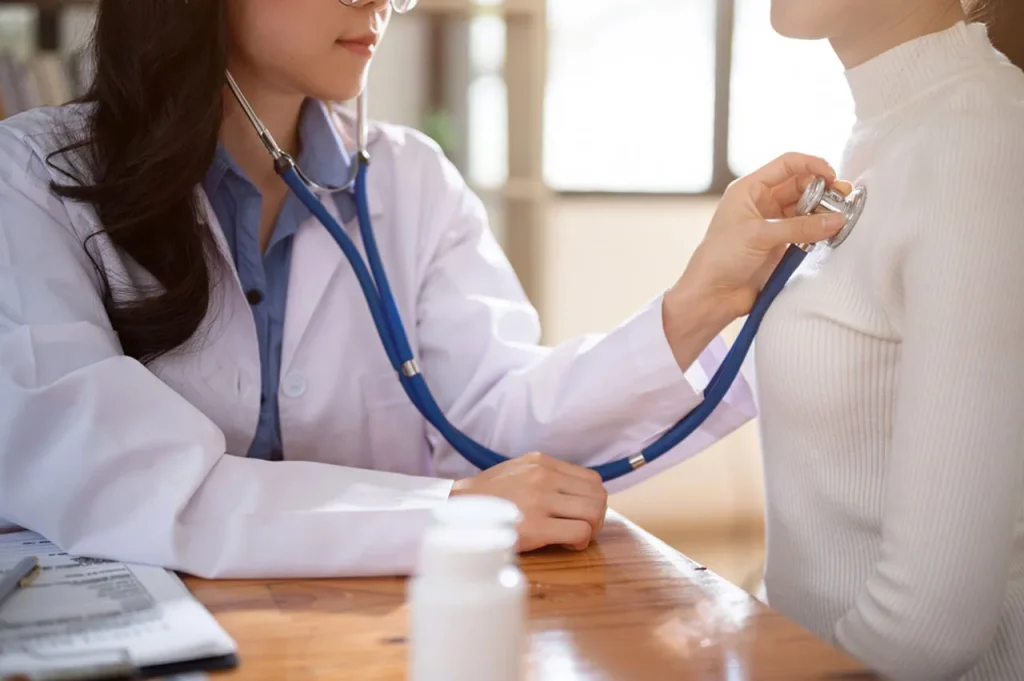 A female doctor uses a stethoscope to check a patient's heart and lungs during a routine annual physical exam.