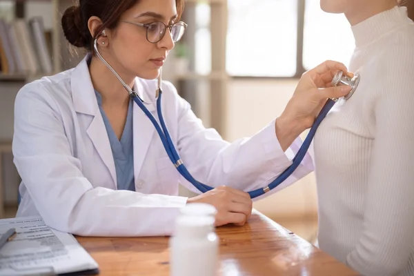 A female doctor uses a stethoscope to check a patient's heart and lungs during a routine annual physical exam.