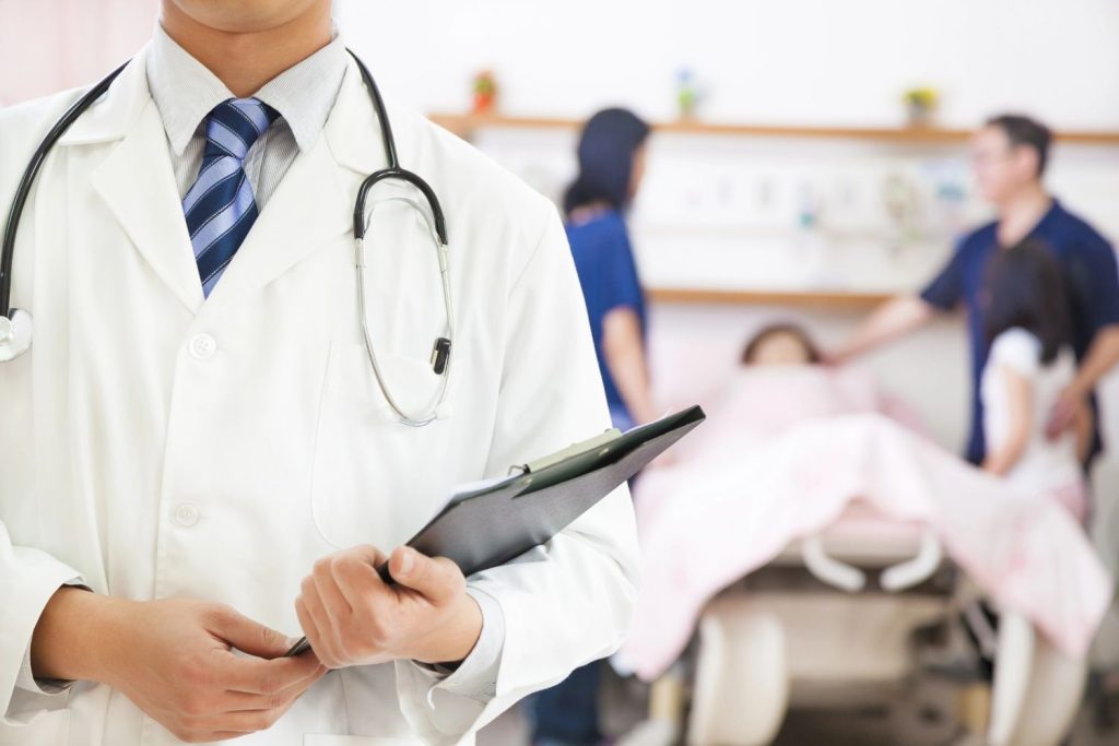 A physician at an immediate care clinic Houston holds a clipboard while medical staff assist a patient in the background.
