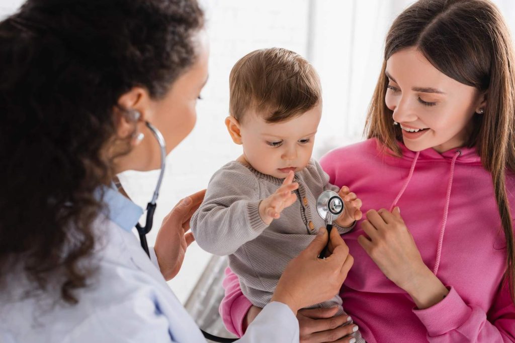 A friendly doctor at an immediate care clinic Houston uses a stethoscope to examine a toddler during a wellness visit.