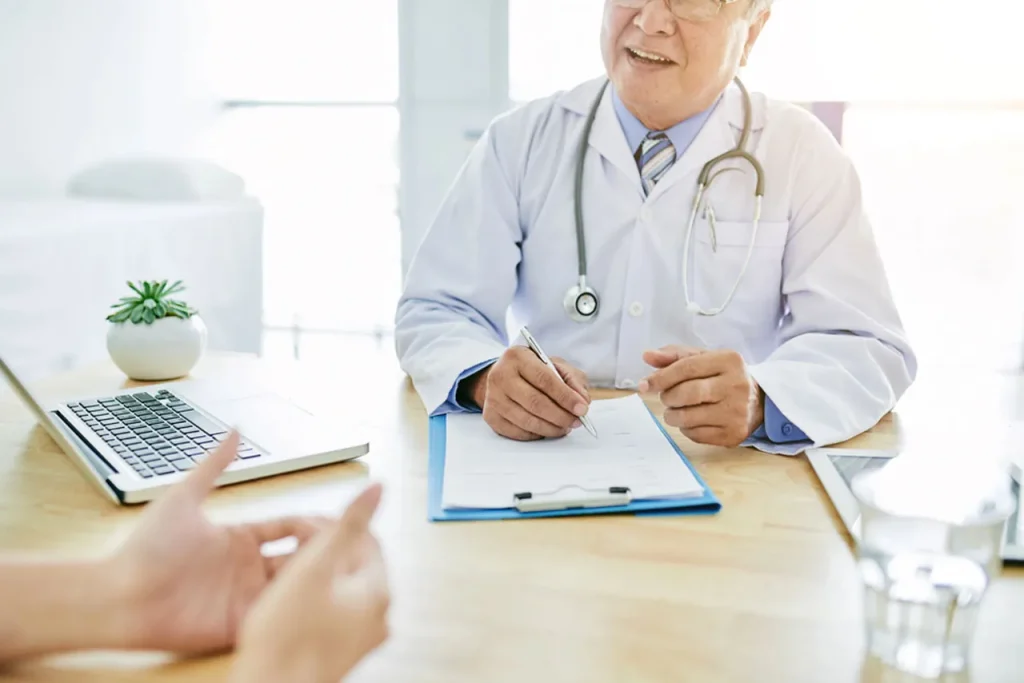 A smiling older doctor takes notes while discussing health goals during a comprehensive annual physical exam.