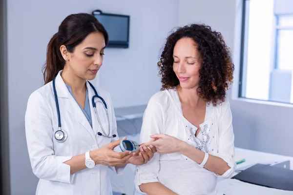Female primary care doctor checking a patient's blood sugar levels.