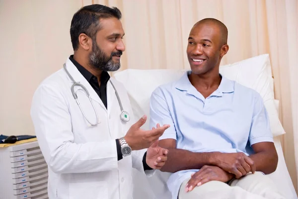 Male primary care doctor speaking with a patient in an exam room.