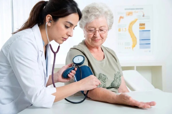 Female primary care doctor checking the blood pressure of a senior patient.